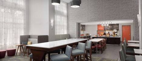 A modern dining area with a long table, bar stools, and a kitchen in the background.