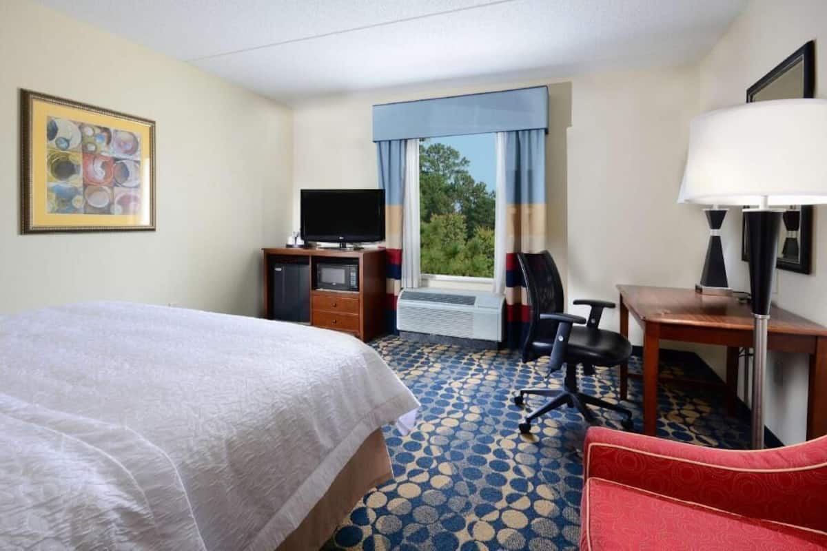 Ein Hotelzimmer mit einem Bett, einem Schreibtisch mit Stuhl, einem Fernseher und einem Fenster mit Vorhängen.