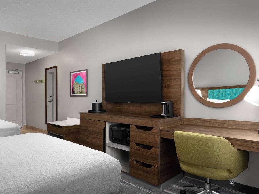 A hotel room with a bed, a desk with a chair, a flat-screen TV, a microwave, and a mirror.