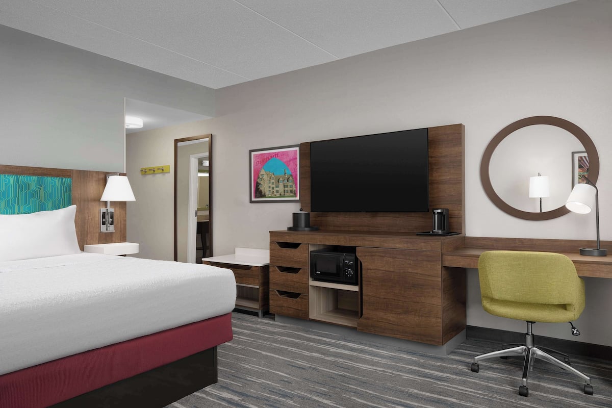 Ein Hotelzimmer mit Bett, Schreibtisch, Stuhl, Fernseher und Mikrowelle.