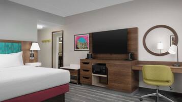 A hotel room with a bed, a desk, a chair, a TV, and a microwave.