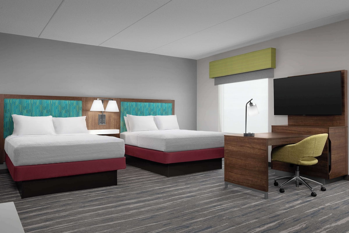 Ein Hotelzimmer mit zwei Betten, einem Schreibtisch und einem Fernseher.