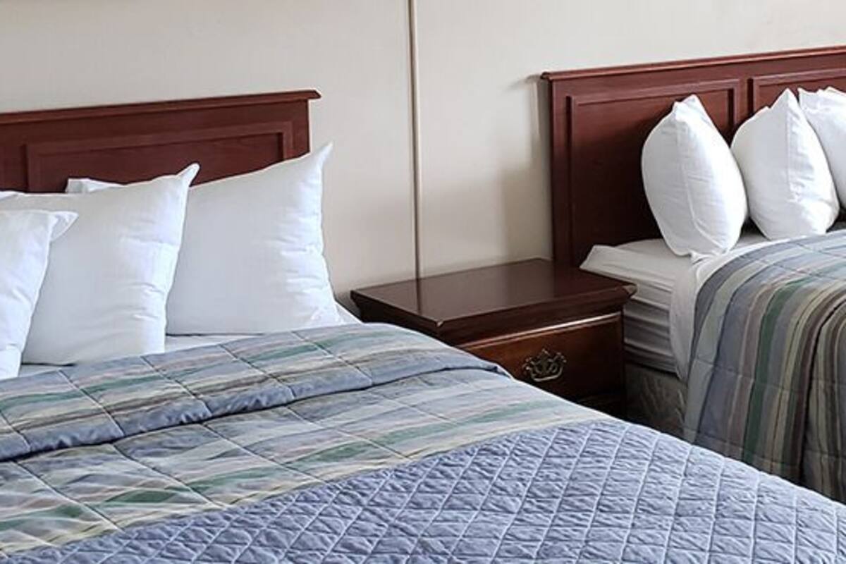 A hotel room with two beds, each with a wooden headboard and white bedding.