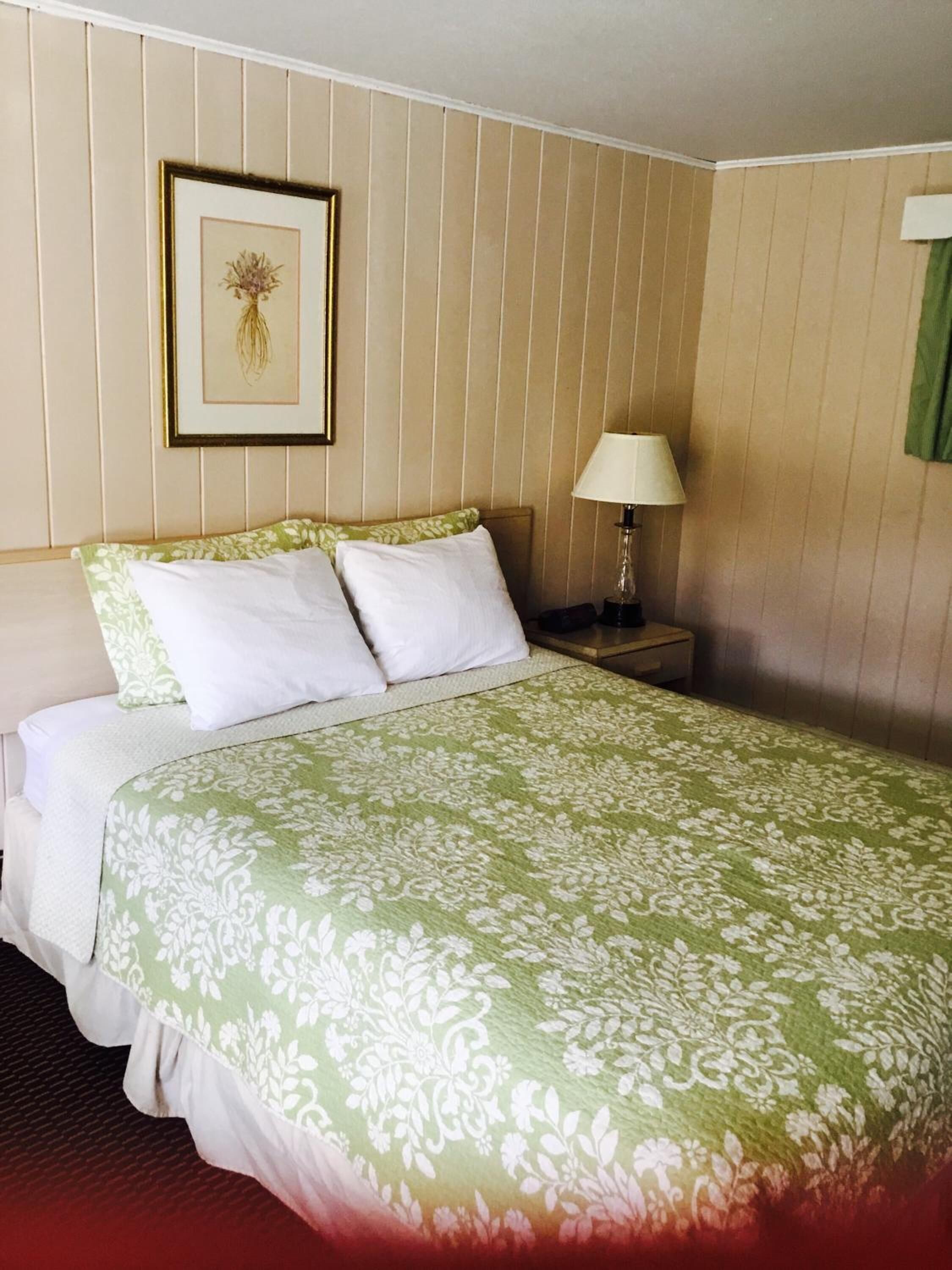 A neatly made bed with a green floral bedspread, two white pillows, and a framed picture on the wall.
