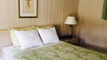 A neatly made bed with a green floral bedspread, two white pillows, and a framed picture on the wall.