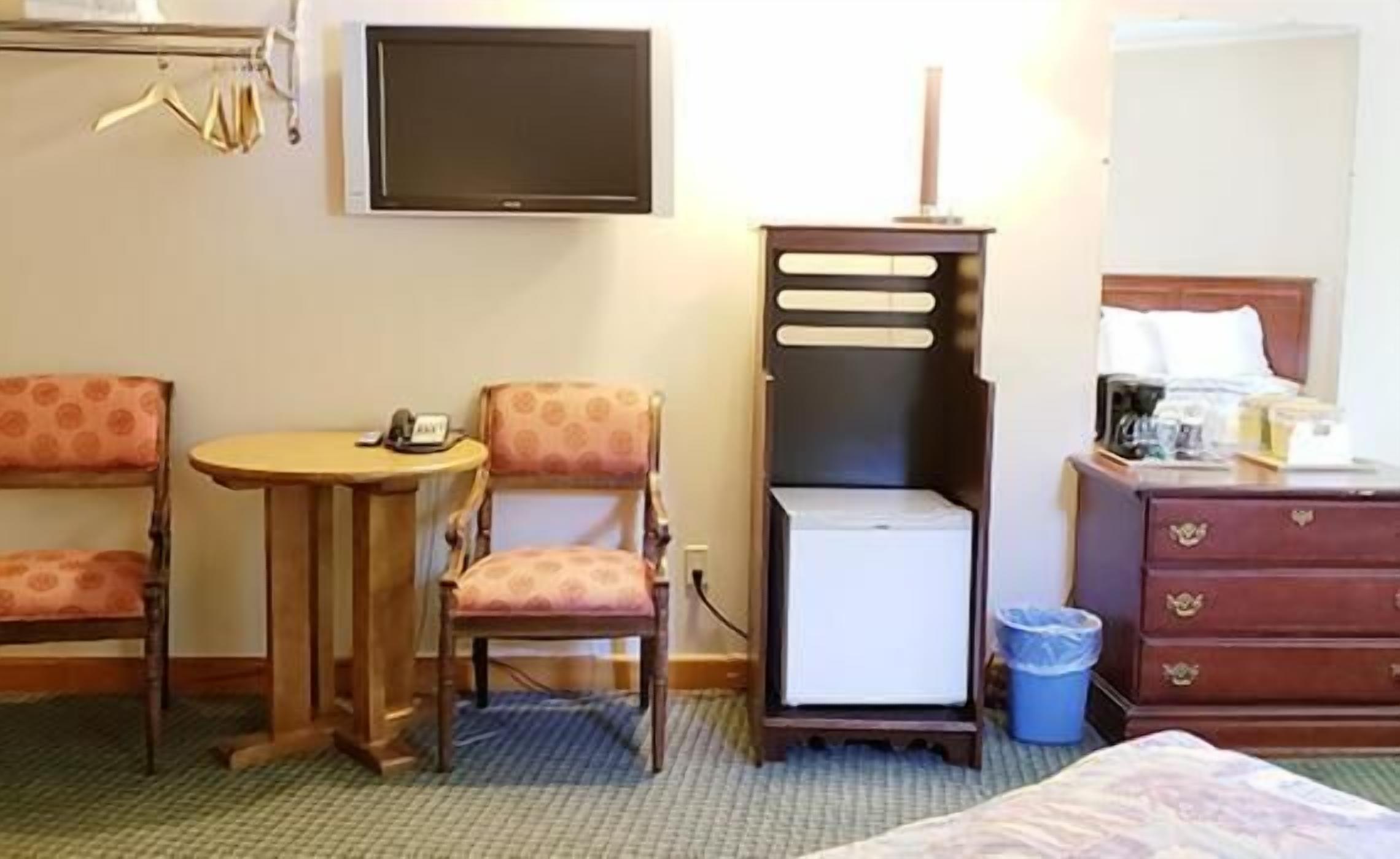 Ein Hotelzimmer mit einem Bett, einem Schreibtisch mit Stuhl, einem Fernseher, einer Kommode und einem Mülleimer.
