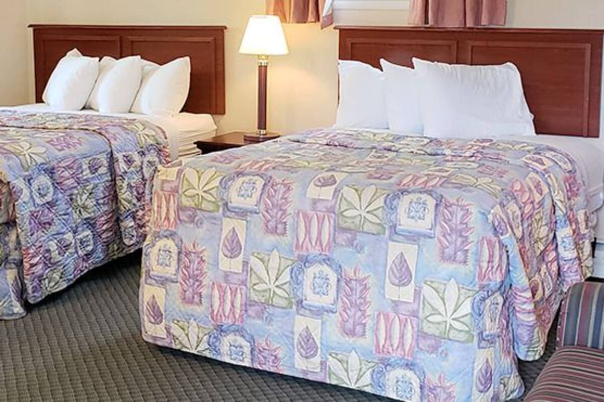 A hotel room with two beds, a wooden headboard, a striped couch, and a lamp.