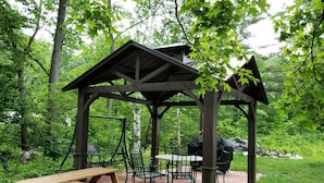 Un belvédère en bois, avec une table et des chaises, entouré de verdure.