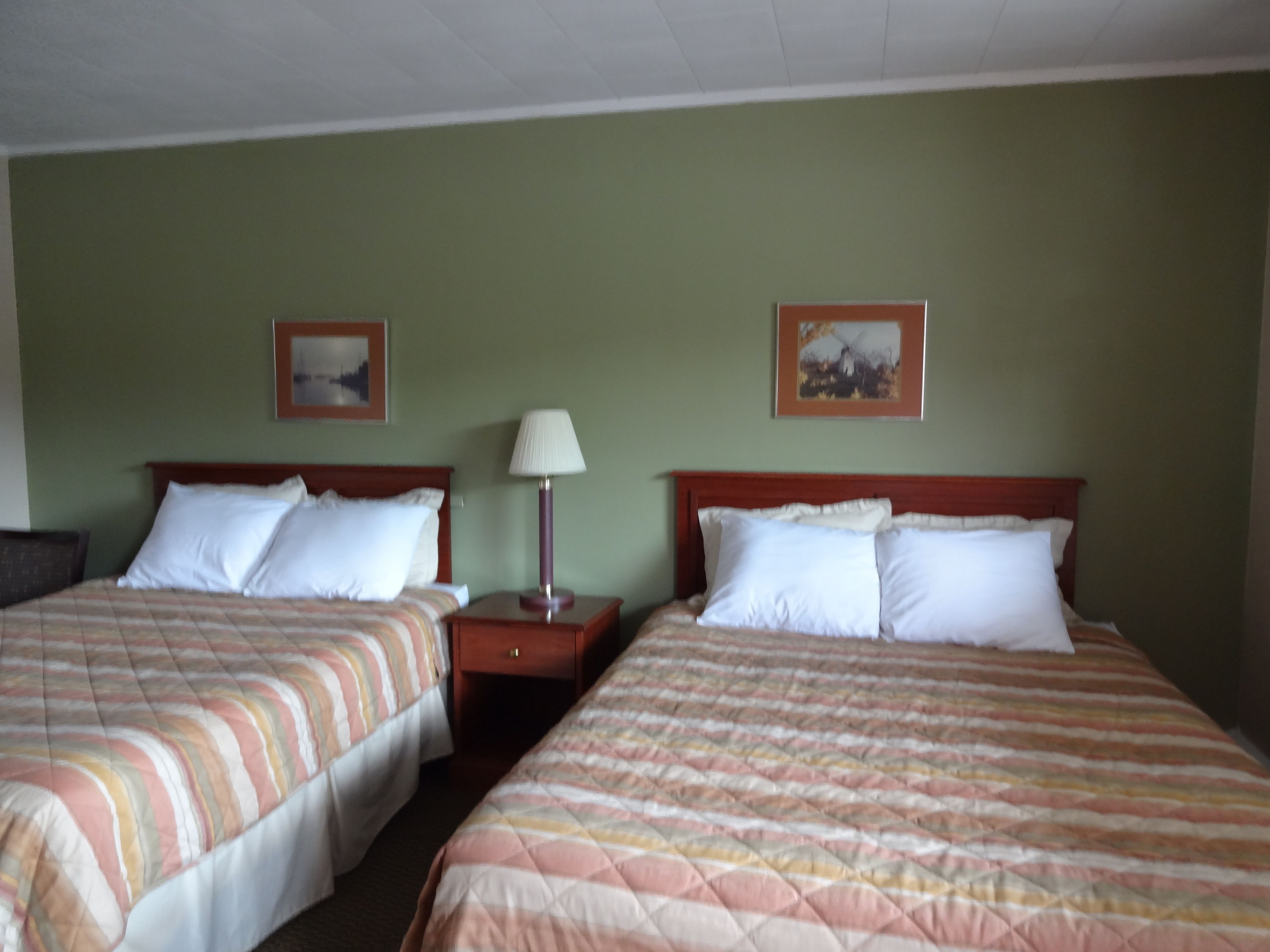 A hotel room with two beds, each with a striped bedspread, a nightstand with a lamp, and two framed pictures on the wall.