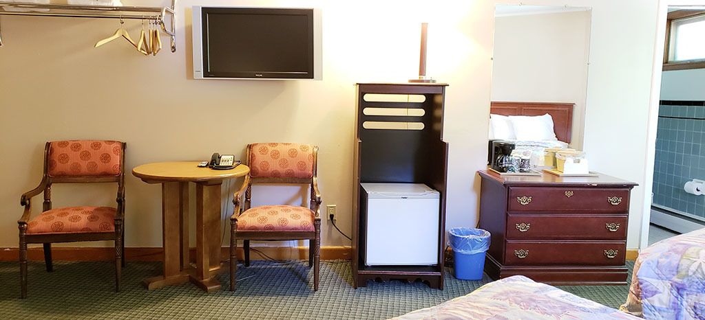 A hotel room with two armchairs, a small table, a minibar, a dresser, and a television on the wall.