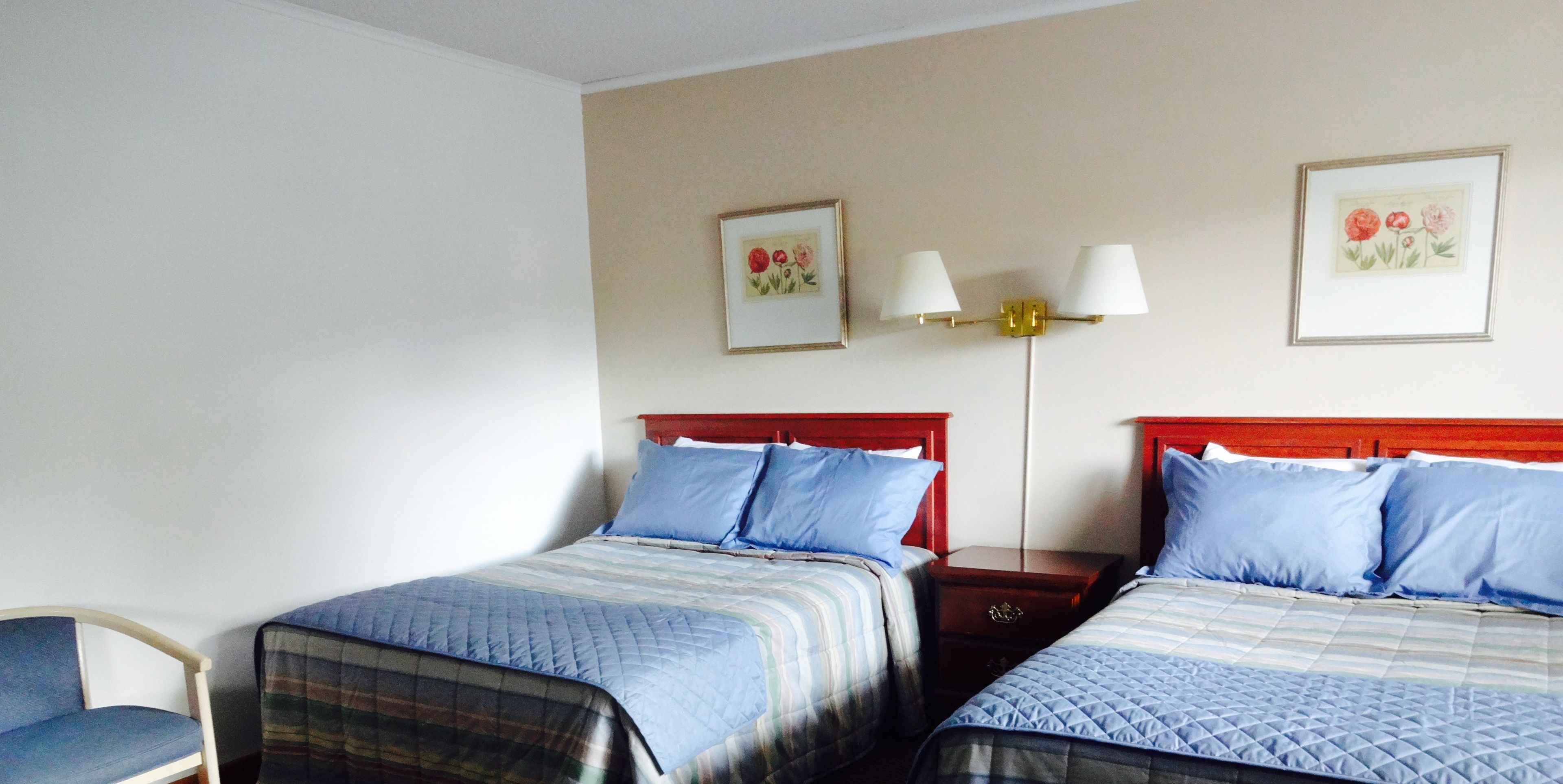 Une chambre d’hôtel avec deux lits, une chaise et deux tables de chevet avec des lampes.