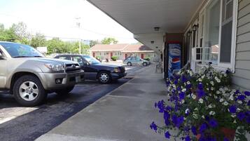 Un motel con área de estacionamiento techada, un anuncio de Pepsi y una jardinera con flores azules y blancas.