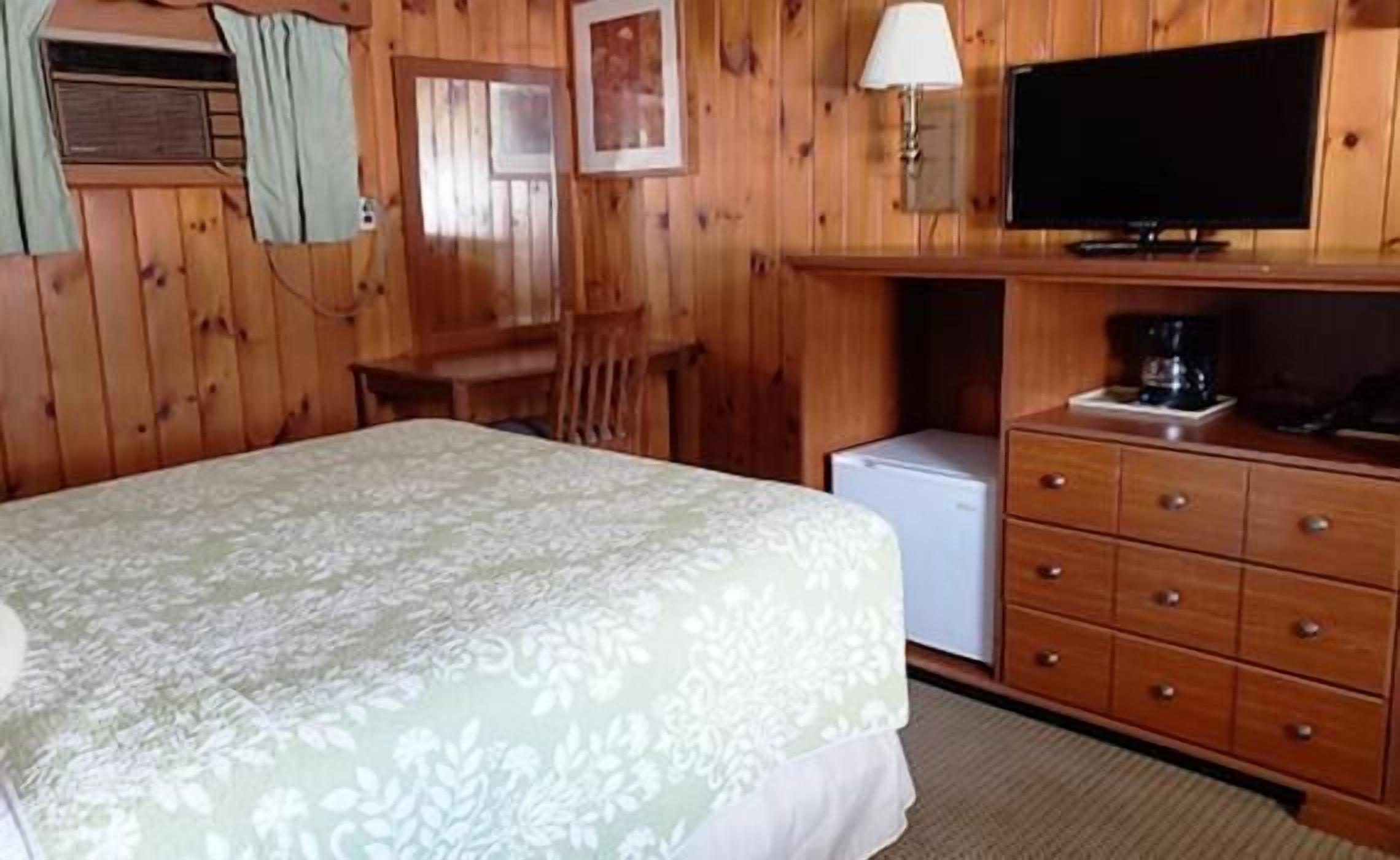A wooden room with a bed, a desk, a television, and a refrigerator.