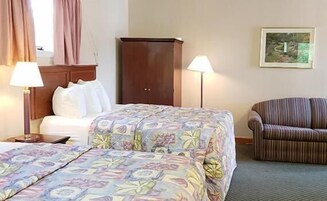 A hotel room with a bed, a wooden wardrobe, a striped armchair, and a painting on the wall.