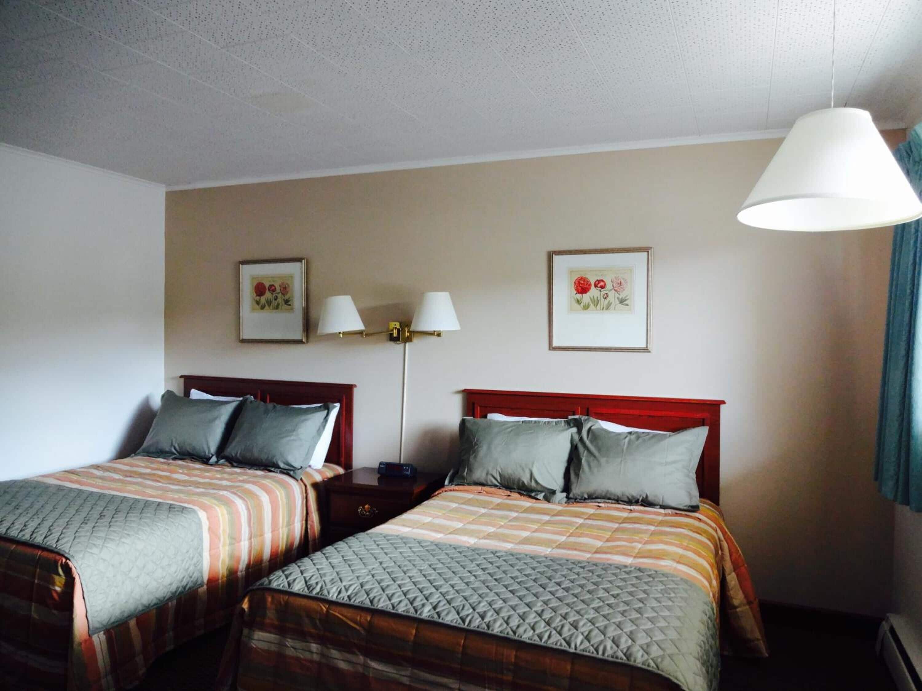 A hotel room with two single beds, a nightstand, a lamp, and two framed floral pictures on the wall.