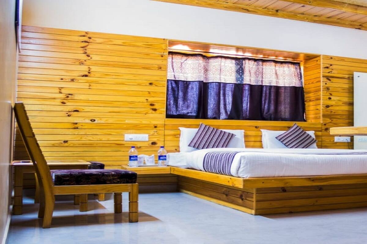 Ein Zimmer mit Holzwänden, einem Bett, einem Sessel und einem Fenster mit Vorhängen.