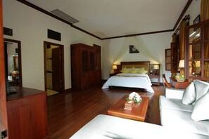 A hotel room with a large bed, a sofa, a wooden coffee table, and a desk with a lamp. - Sokhalay Angkor Villa Resort (Siem Reap)
