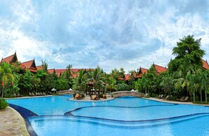 A large outdoor swimming pool with multiple sections, surrounded by palm trees and a building with red roofs. - Sokhalay Angkor Villa Resort (Siem Reap)