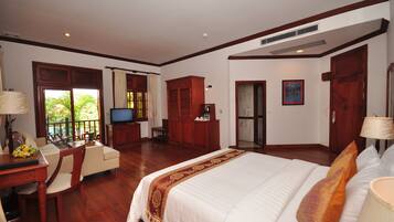 Habitación de hotel con una cama grande, un escritorio con televisor, un balcón con vistas y muebles de madera.