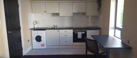 A compact kitchen with a washing machine, a small oven, and a dining area with a table and chair.