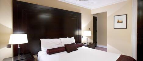 Habitación de hotel con una cama grande, dos mesitas de noche con lámparas, un cabecero de madera oscura y un cuadro en la pared.