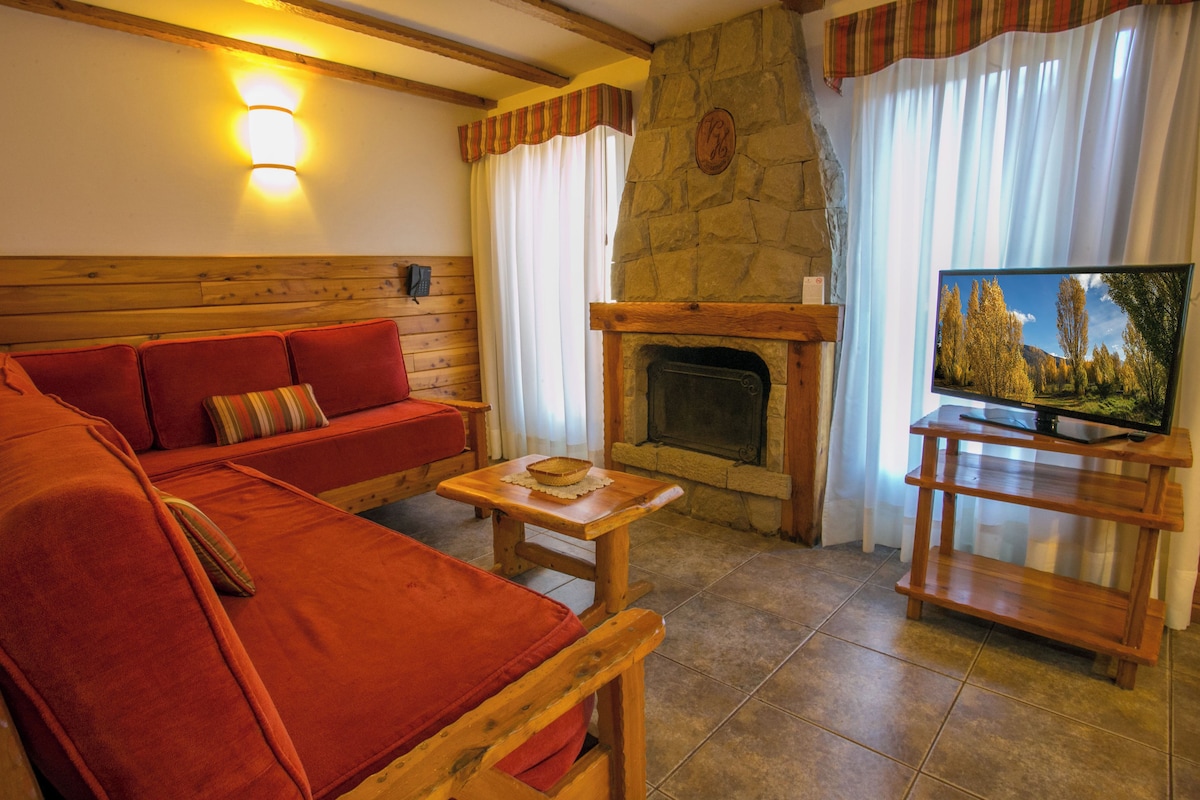 Een gezellige woonkamer met een stenen openhaard, een rode bank, een houten salontafel en een televisie op een houten dressoir.