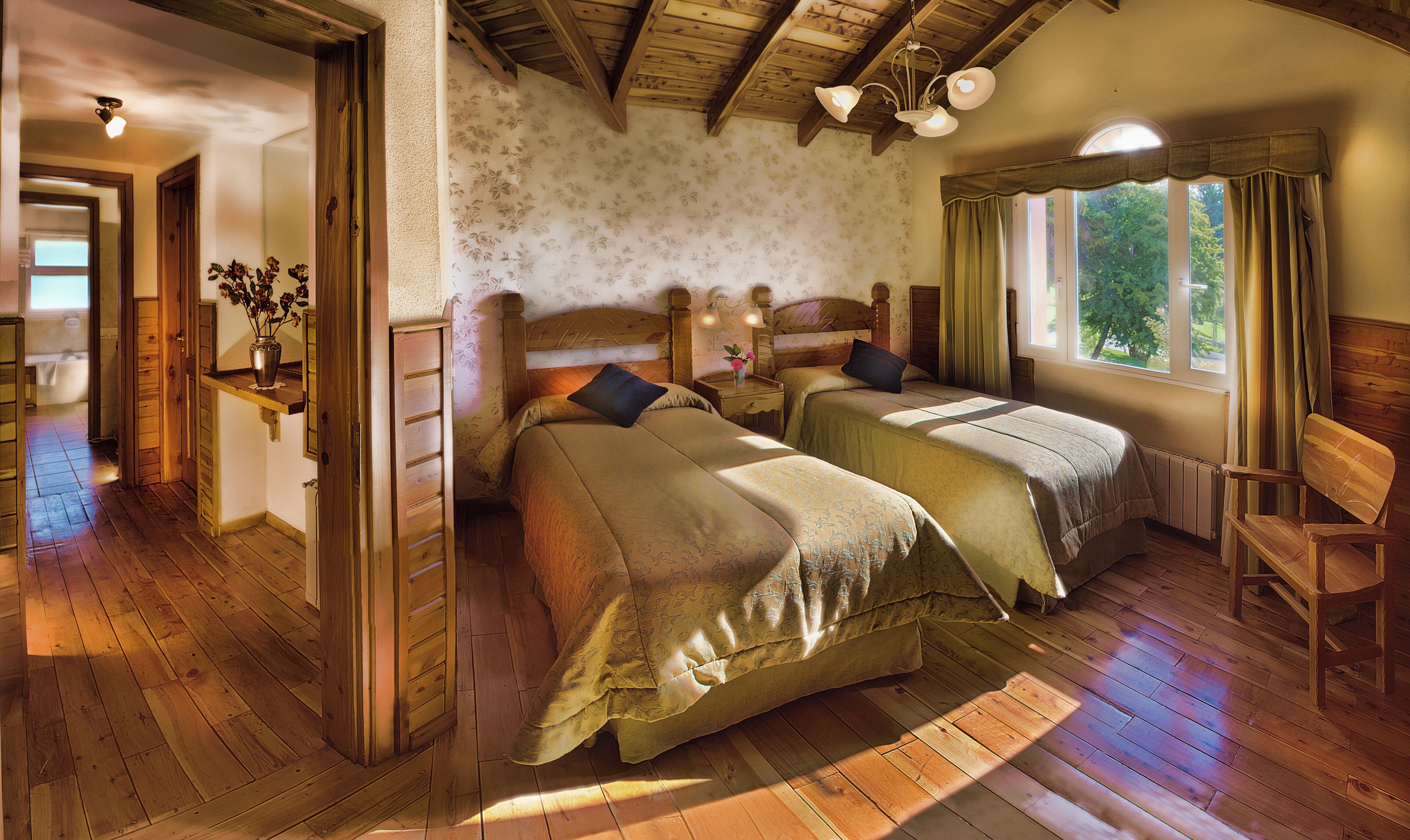 A room with two wooden beds, a wooden chair, a nightstand with a lamp, a window with curtains, and a wooden ceiling.