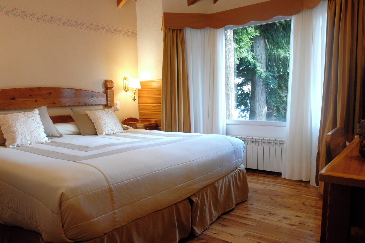 A large bed with a wooden headboard, a nightstand, a lamp, and a window with curtains.
