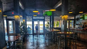 Un interno ristorante con tavoli e sedie, una zona bar e vista sull'esterno.
