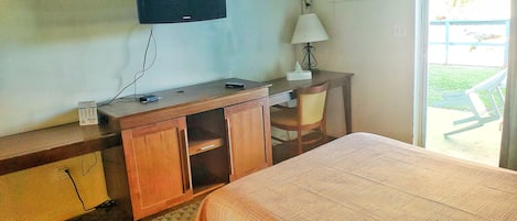 Habitación de hotel con cama, escritorio con computadora, televisor montado en la pared y ventana con vista al exterior.
