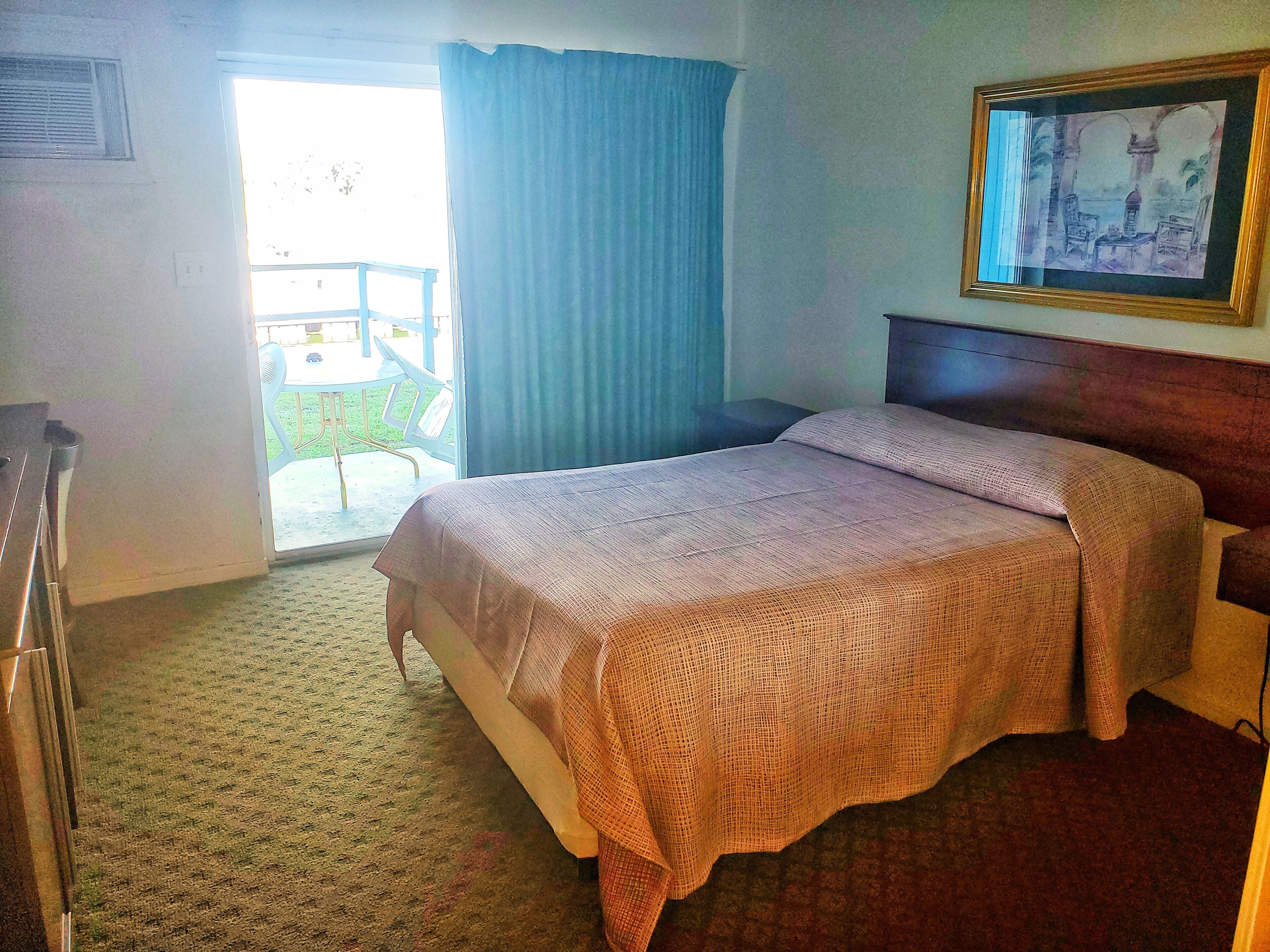 A hotel room with a bed, a painting on the wall, and a view of the outside.