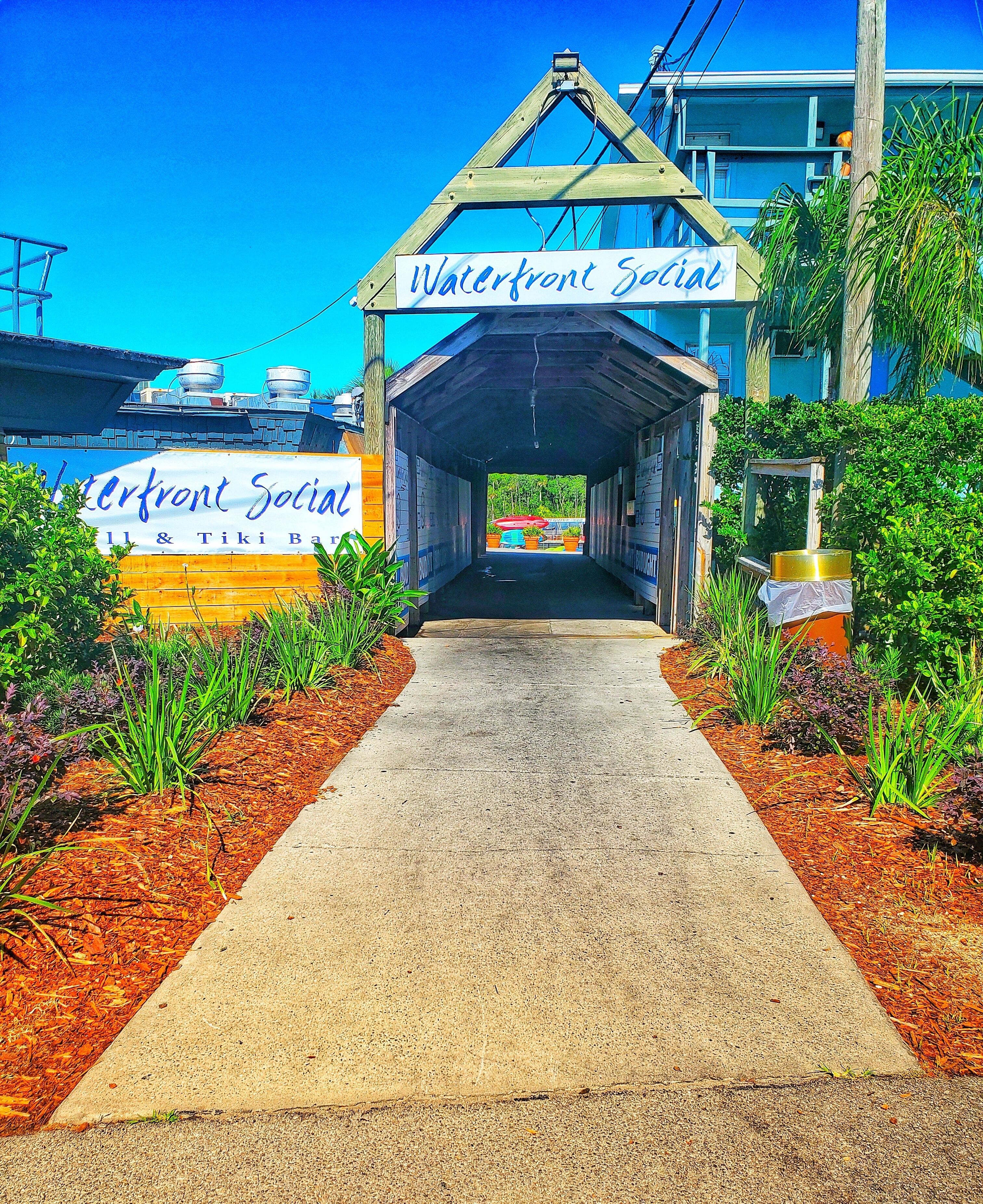 A pathway leading to a building with a sign reading "Waterfront Social & Tiki Bar."