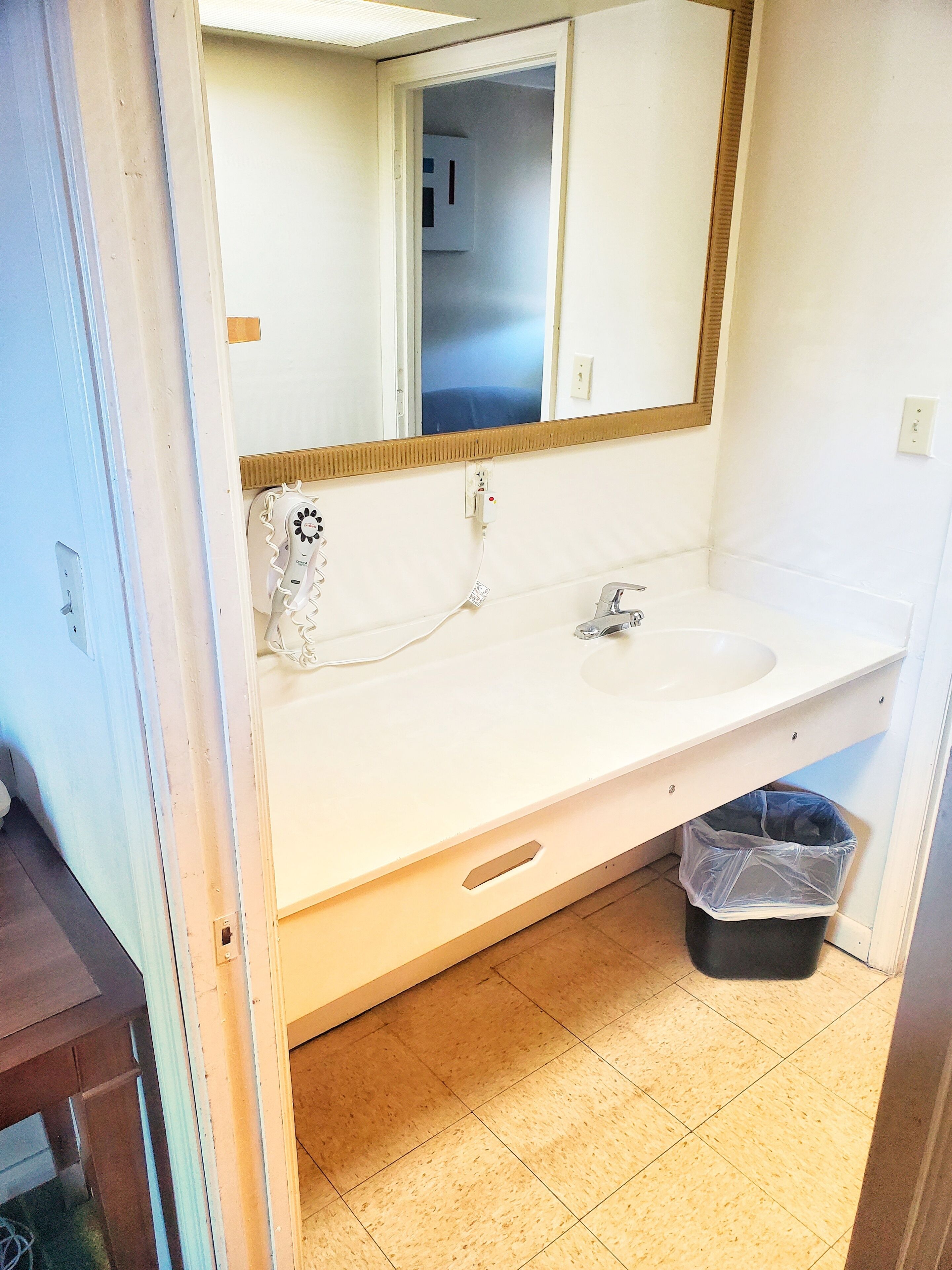 A bathroom with a white sink, a mirror, and a trash bin.