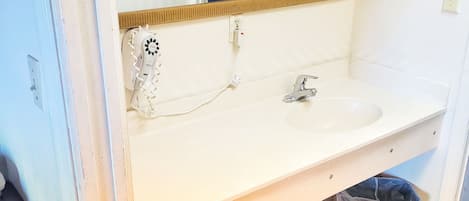 Un baño con un lavamanos blanco, un espejo y un cubo de basura.