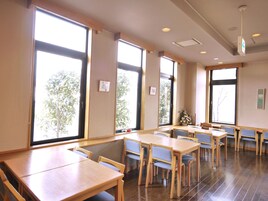 Un amplio comedor con mesas y sillas de madera, ventanas grandes e iluminación empotrada en el techo.