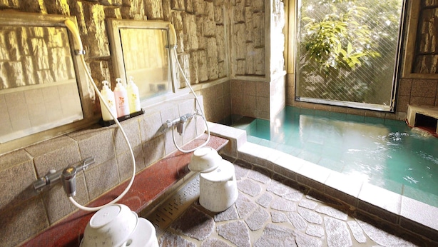 A stone-walled bathroom with a bathtub, a window, and a shower area. - Hotel Route-Inn Nagaizumi Numazu Inter 2 (Nagaizumi)