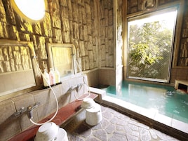 A stone-walled bathroom with a bathtub, a window, and a shower area.
