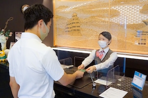 A reception desk with a glass partition, a framed artwork of a pagoda, and a small table with a calendar and a phone.