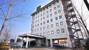 A multi-story hotel with a modern architectural design, featuring a large entrance with a covered area and a parking lot in front. - Hotel Route-Inn Nagaizumi Numazu Inter 2 (Nagaizumi)