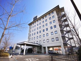 A multi-story hotel with a modern architectural design, featuring a large entrance with a covered area and a parking lot in front.