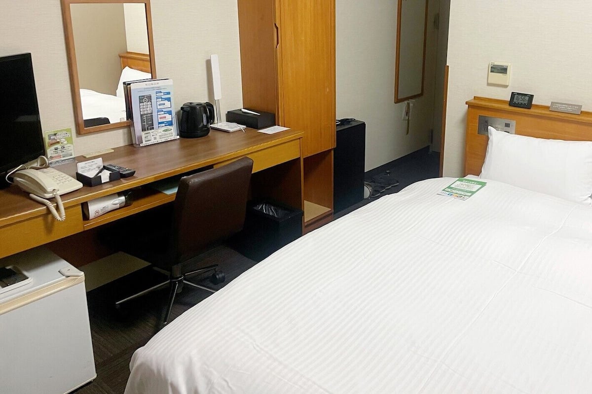 A hotel room with a bed, a desk with a computer, a telephone, and a mirror.