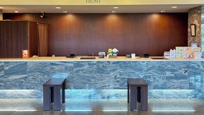 A hotel reception area with a marble counter, two wooden stools, a wooden wall, and an emergency exit sign. - Hotel Route-Inn Omaezaki (Omaezaki)