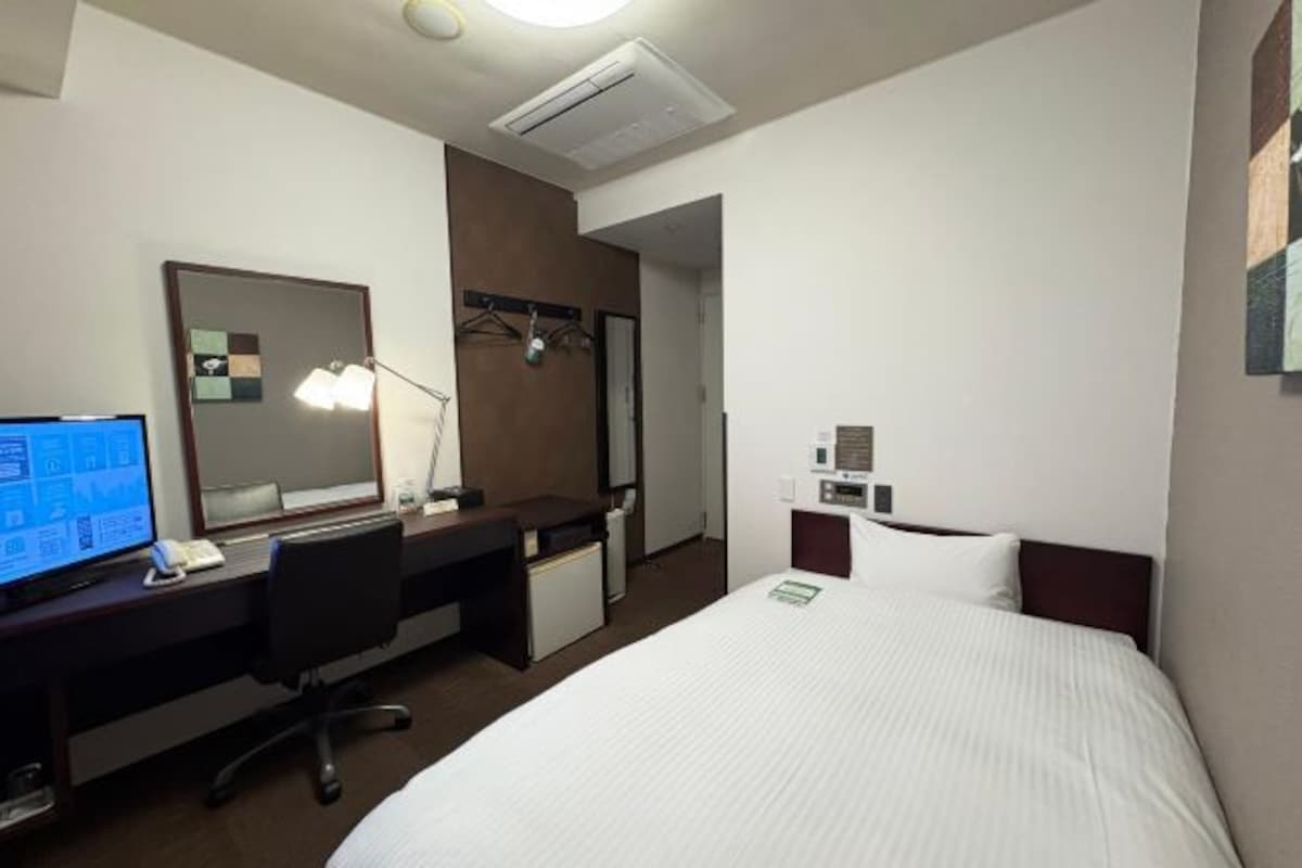 A hotel room with a bed, desk, computer, and a mirror.
