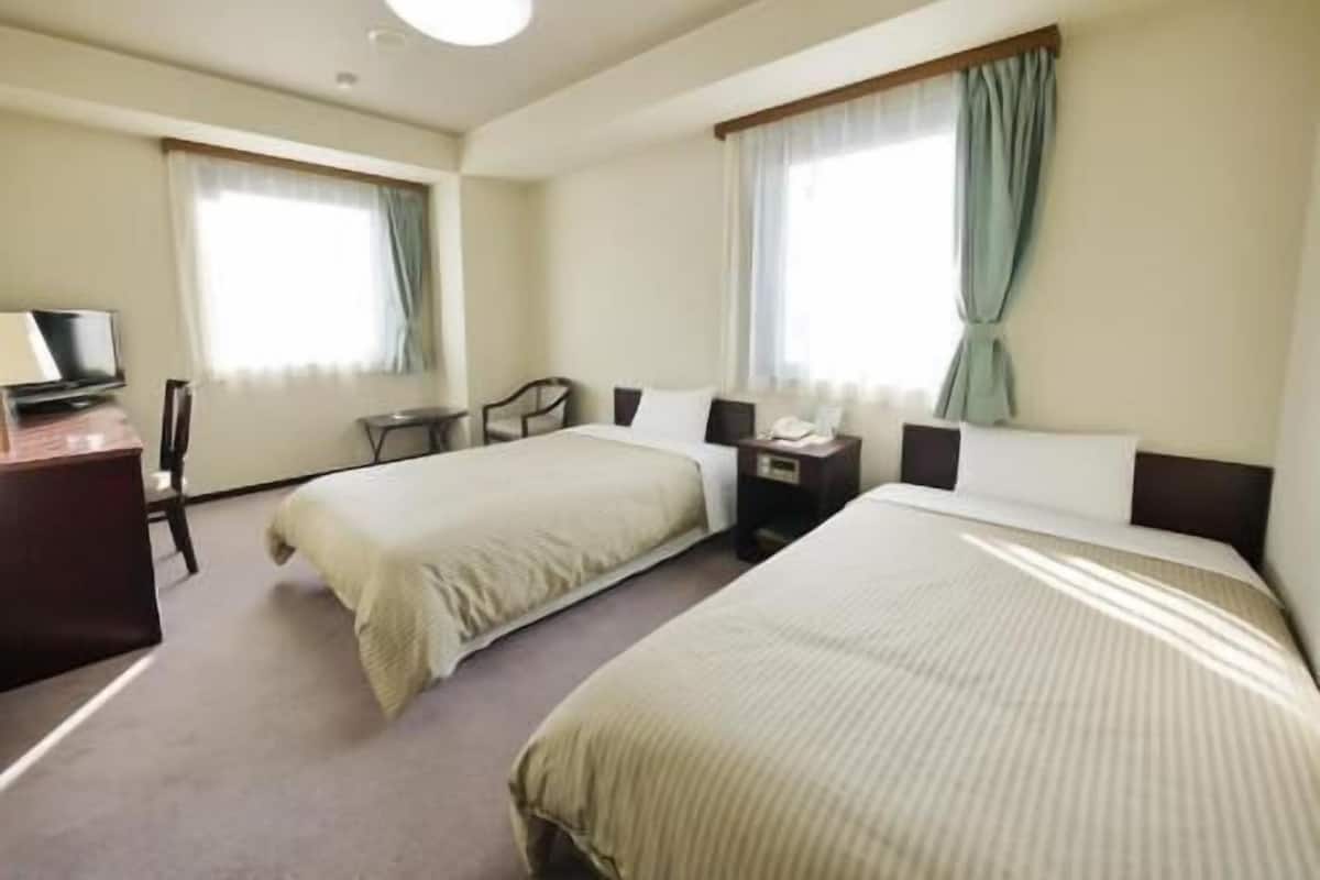 A hotel room with two beds, a desk, a chair, a TV, and a window with curtains.