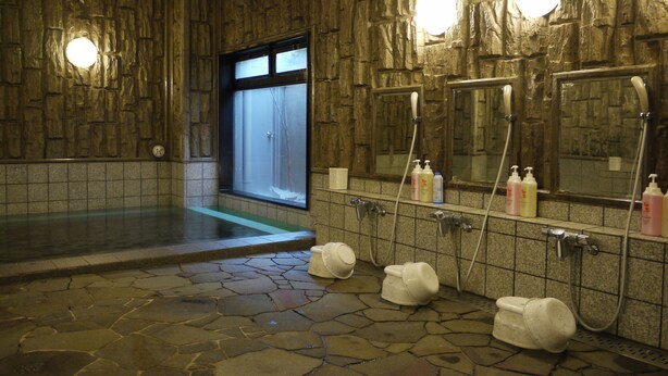 A stone-floored bathroom with a large bathtub, a shower area, and a mirror with multiple hand dryers. - Hotel Route Inn Shimada Ekimae (Shimada)