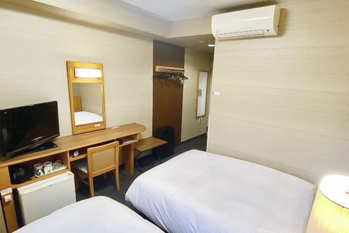 Habitación de hotel con dos camas, un escritorio, televisor, espejo y aire acondicionado.