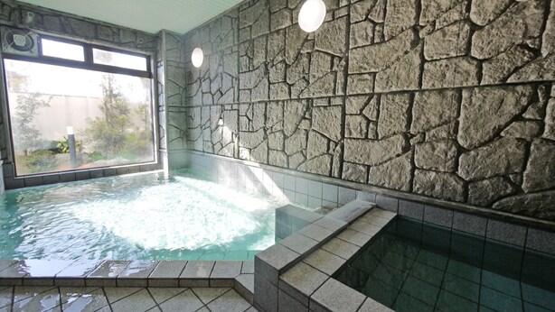 A stone-walled indoor pool with clear water, tiled flooring, and a view of greenery outside. - Hotel Route-Inn Shimada Yoshida Inter (Shimada)