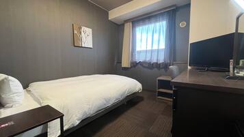 Una habitación de hotel con una cama individual, un escritorio con una computadora, un televisor y una ventana con cortinas.