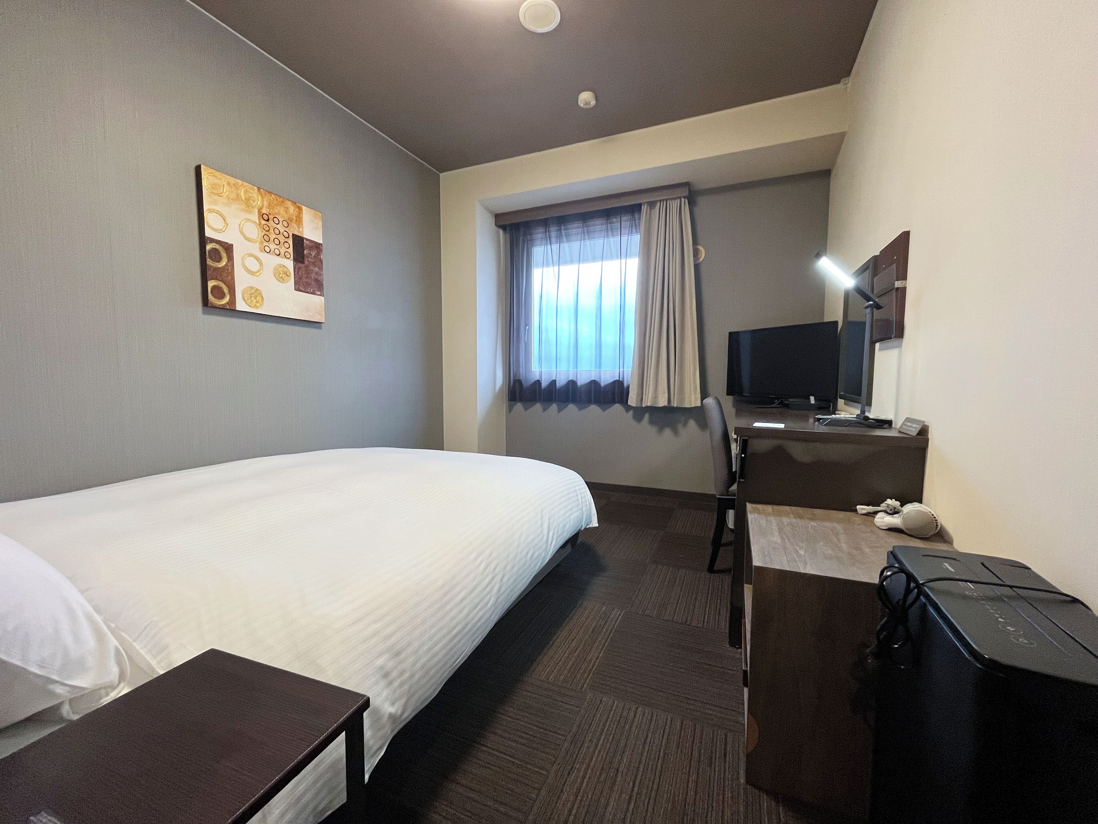 Habitación de hotel con una cama grande, un escritorio con computadora, un televisor y una ventana con cortinas.