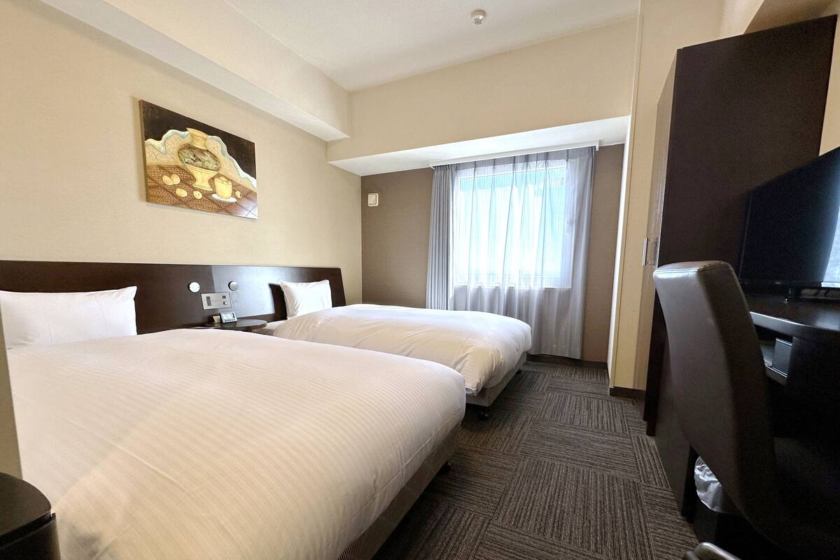 A hotel room with two beds, a television, a desk, and a painting on the wall.